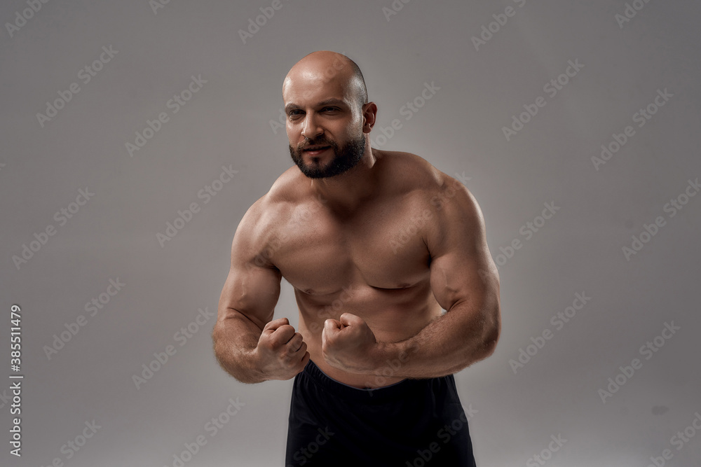 Fototapeta premium Strength. Muscular strong caucasian man bodybuilder showing his perfect body, chest, biceps, abs while posing shirtless isolated over grey background