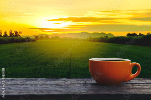 Hot coffee cup Ceramic brown glass placed on an outdoor old wood table. The background is a landscape of nature with mountains and rice field