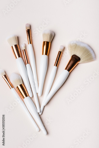 top view of white and golden cosmetic brushes set on beige background