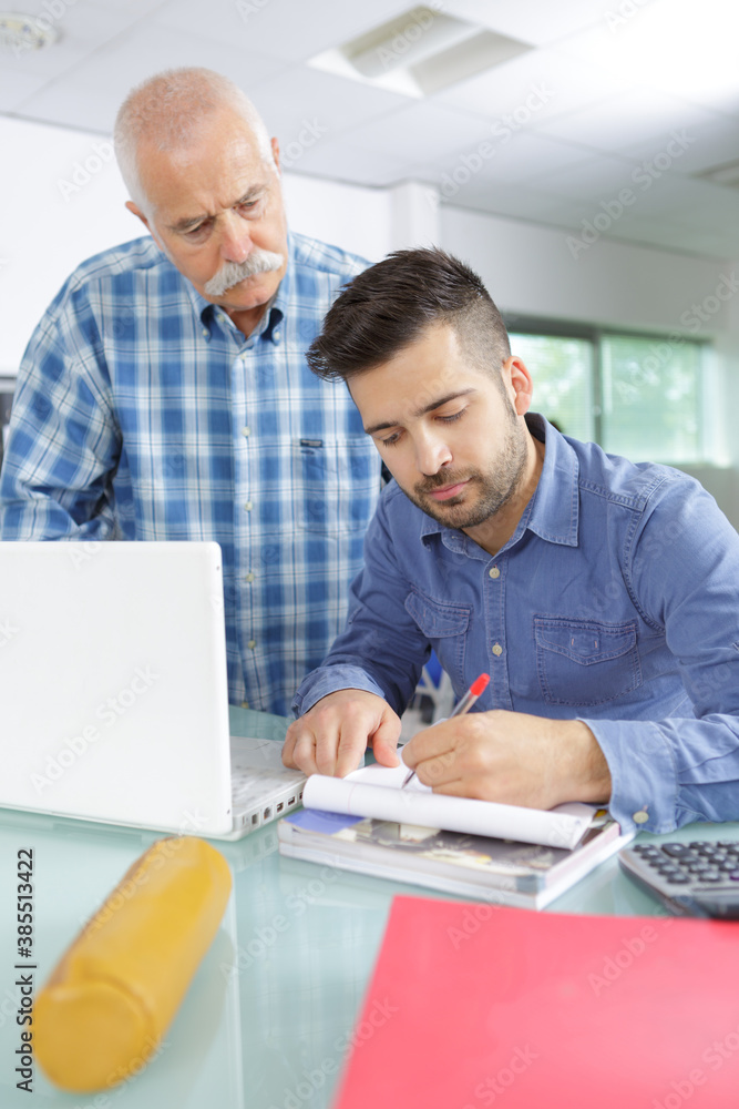 Senior man watching younger man writing Senior man watching younger man writing