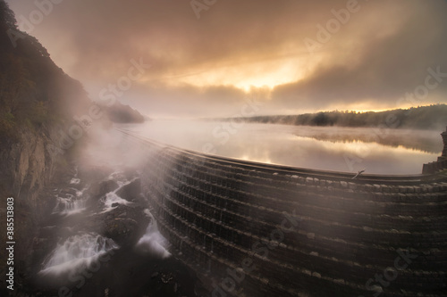 Ethereal moody sunrise with low fog and steam being illuminated over a lake and waterfall. Croton Gorge, New York