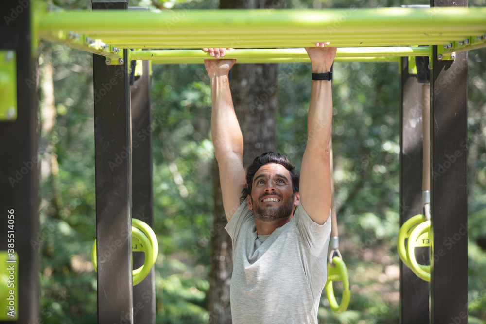 Obraz premium man doing abdominal exercise on horizontal bar in summer park