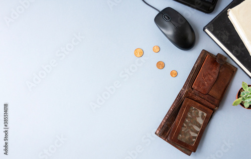 Unemployment concept. A lack of money. Coins fall out of a wallet on a gray background with copy space. There are books, a computer mouse, a keyboard nearby