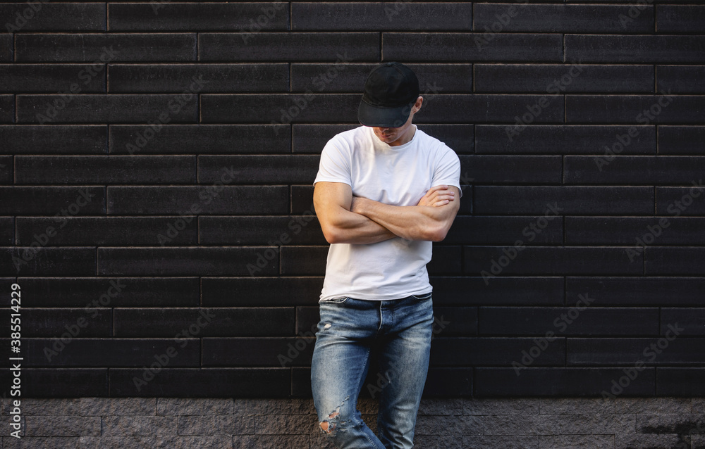 Man in white t-shirt standing against brick wall with arms crossed