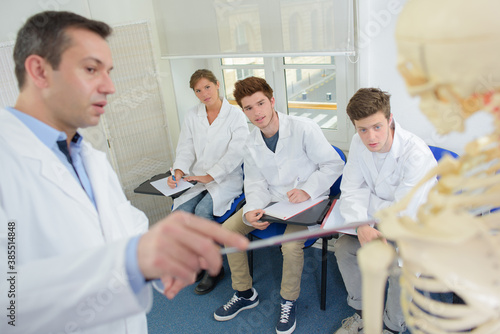 Teacher pointing to skeleton while giving lecture to students
