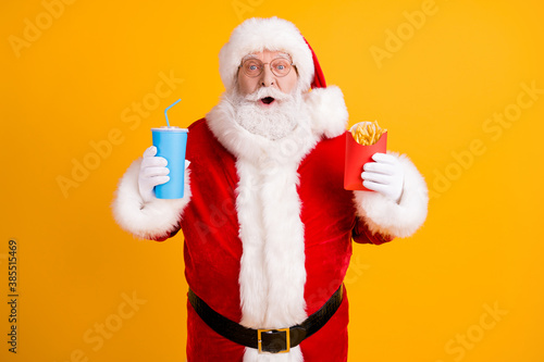 Portrait of his he nice cheerful stunned amazed funny white-haired Santa eating fastfood menu recipe meal dish sale discount isolated over bright vivid shine vibrant yellow color background
