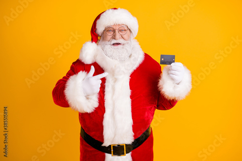 Photo fat white grey hair beard santa claus point finger credit card best choice x-mas eve noel christmas magic party purchase wear cap headwear isolated bright shine color background