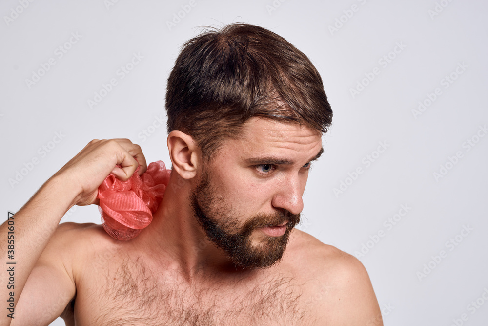 Naklejka premium A man with bare shoulders a washcloth in his hands clean skin taking a shower light background