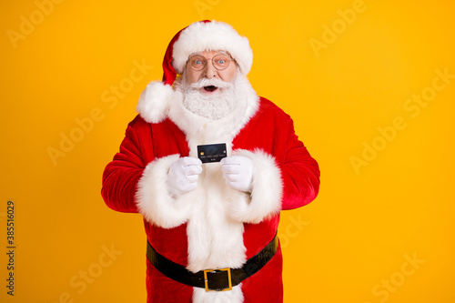Portrait of his he nice cheerful cheery funny amazed glad white-haired Santa holding in hands using black bank card isolated bright vivid shine vibrant yellow color background