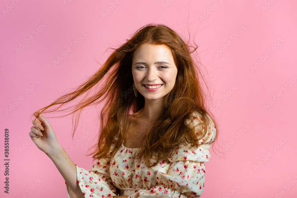 Young woman with long red wavy and shiny hairstyle looking to camera, flirting. Beautiful model girl demonstrate her elegant volume hair. Pink studio background. Young woman with long red wavy and shiny hairstyle looking to camera, flirting. Beautiful model girl demonstrate her elegant volume hair. Pink studio background.