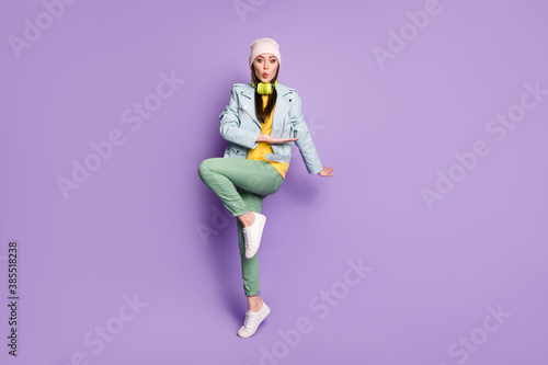 Full length photo of funky attractive lady stylish clothes good mood dance youngster moves raise hands leg rejoicing wear casual hat jacket pants shoes isolated purple color background