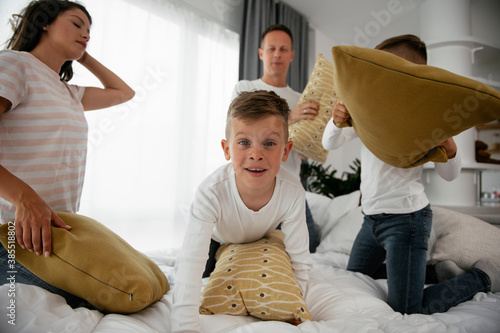 Young parents with sons fighting pillows on the bed. Happy mother and father with boys having fun at home... photo