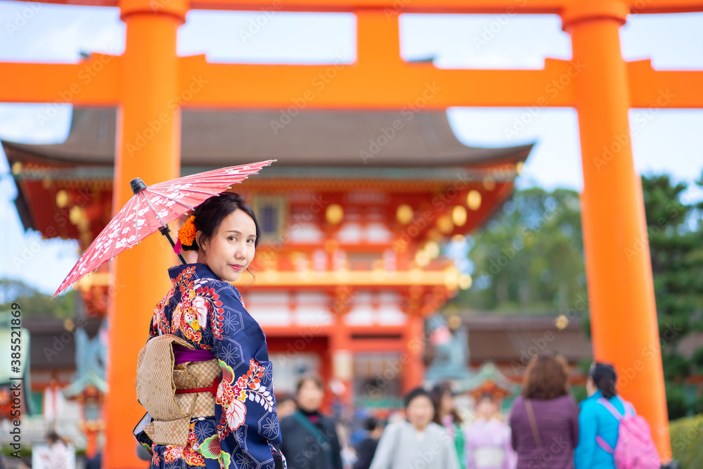 Geishas girl wearing Japanese kimono among red wooden Tori Gate at Fushimi Inari Shrine in Kyoto, Kimono is a Japanese traditional garment. The word 