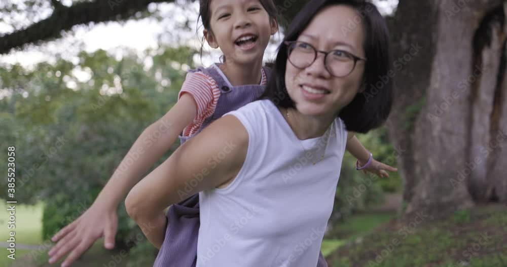Happy little Asian girl getting a piggy back ride from her mother in the park on the morning. Happy little Asian girl getting a piggy back ride from her mother in the park on the morning.