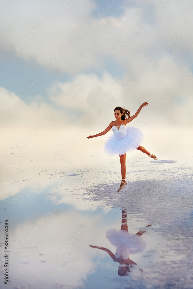 Tender girl ballerina in a white ballet dress in a graceful jump on the lake. Artistic photo.