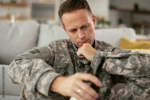 Depressed soldier with bottle sitting in living room. Alcohol addiction..