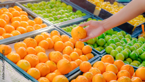Close up hand choosing orange from the food counter at the supermarket.