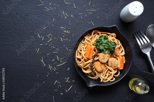 a pan of spahetti with sausage and crab stick on the black wooden table of the italian restaurant during dinner with friends photo