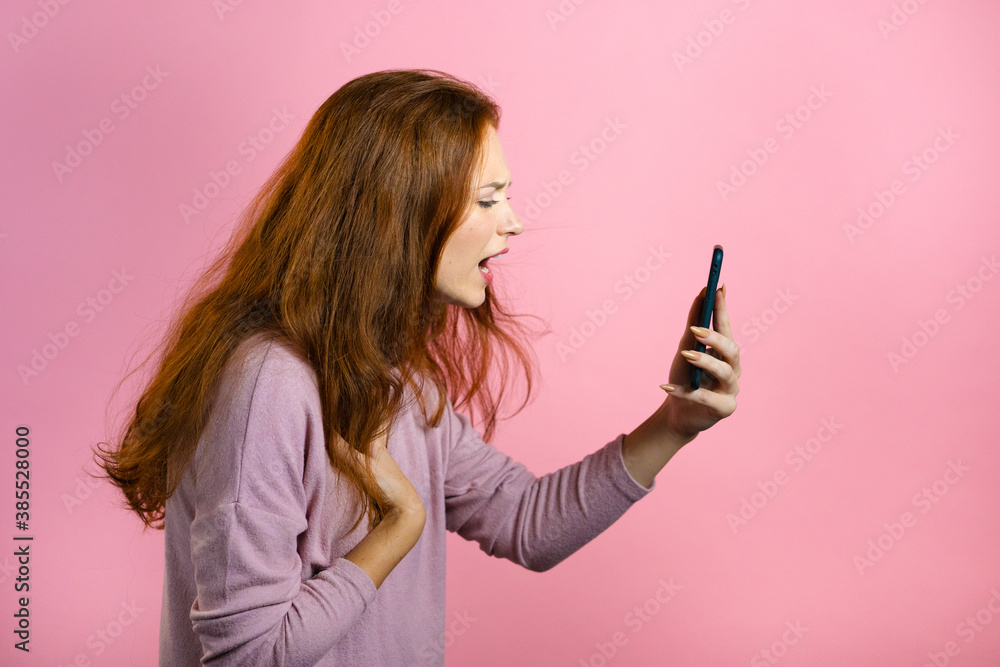 Angry woman screaming down, swears with somebody. Using mobile phone. Stressed and depressed girl on pink background