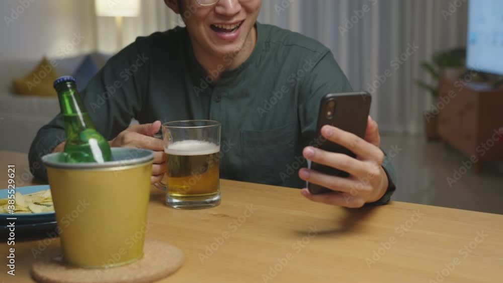 Zoom in : Attractive young happy asian man enjoy relax night party event online celebration festive with friends at house clinking beer with glass and bottle toasting drinking via video call. Zoom in : Attractive young happy asian man enjoy relax night party event online celebration festive with friends at house clinking beer with glass and bottle toasting drinking via video call.