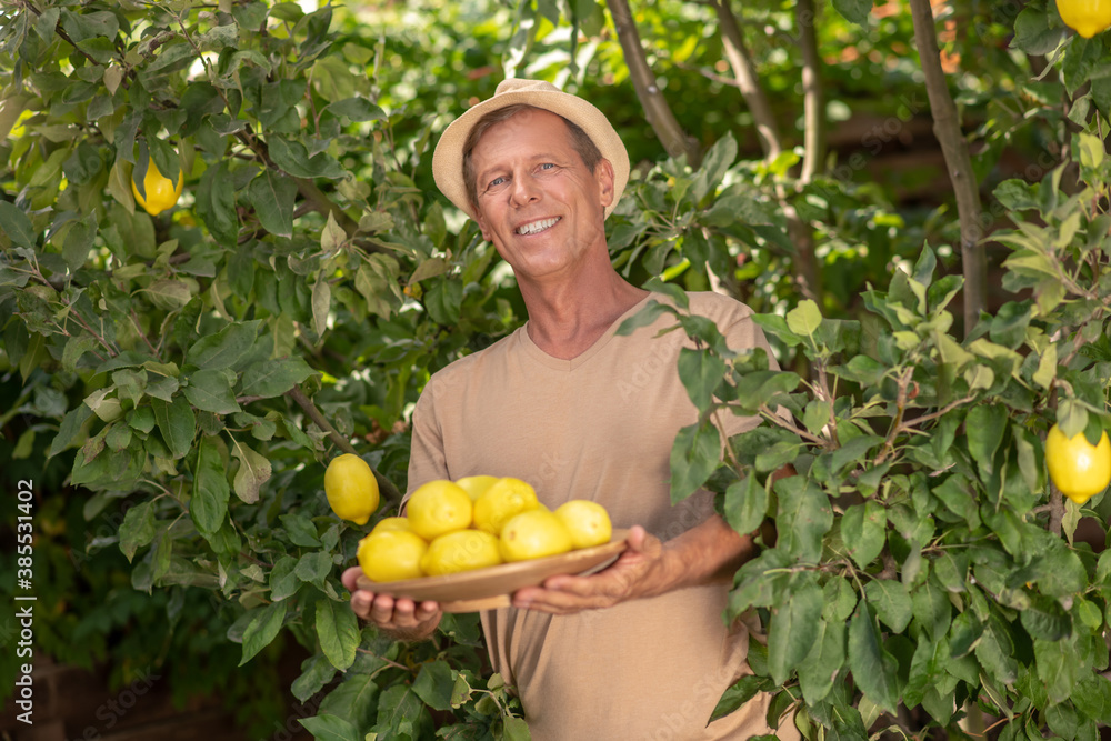 Obraz premium Smiling male in straw hat holding plate with lemons