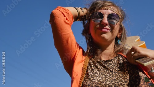 nature, summer vacation, vacation and people concept - happy smiling woman in sunglasses stands with a guitar on her shoulder. photo