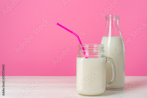 Glass jars with flavoured milkshakes against pink background