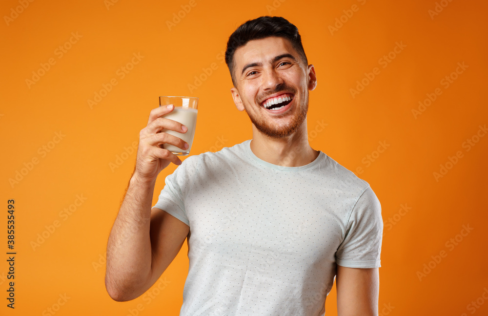 Happy smiling mixed-race man holding milk against yellow background Happy smiling mixed-race man holding milk against yellow background