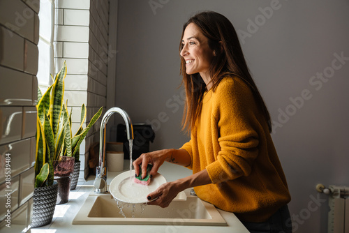 Beautiful middle-aged woman smiling while washing dishes at home photo