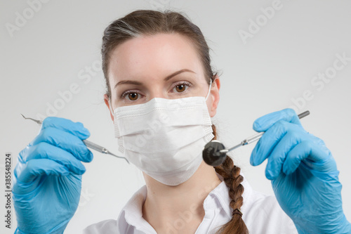 female dentist with dental face mask holds two dental instruments for dental examination