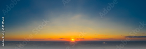 Panoramic image of a warm red sunset with rays of sun over the autumn mist