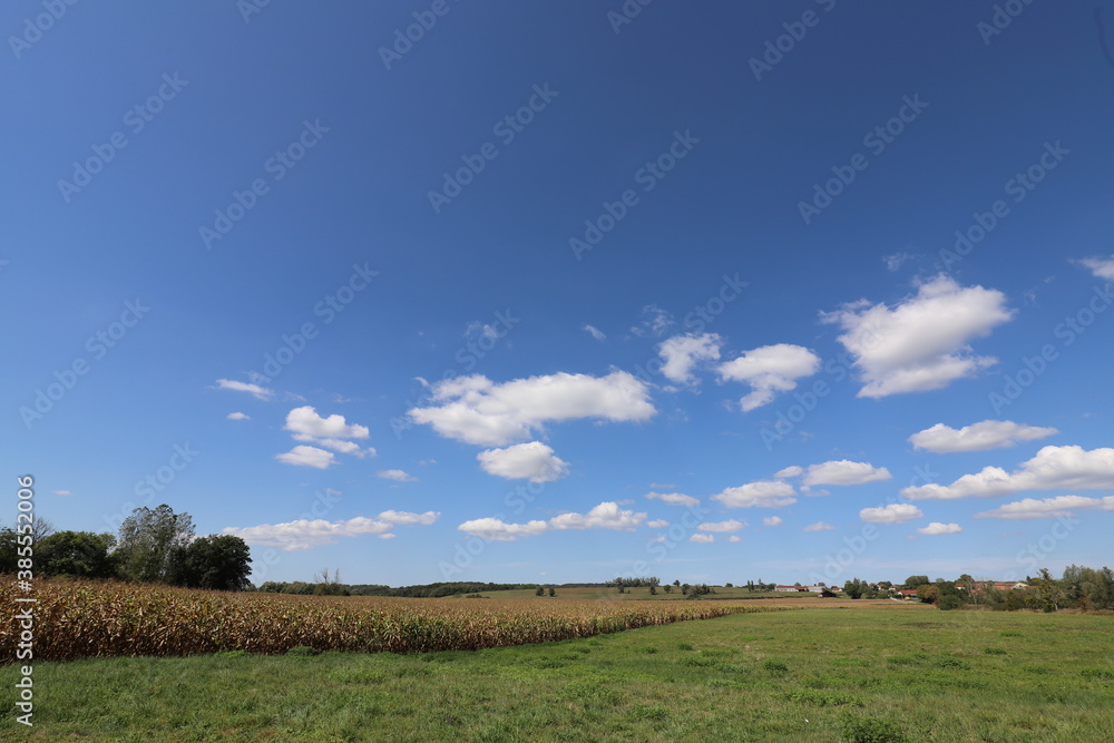 Beautiful panoramic view over a rolling French landscape with agricultural fields and a small village in the distance. Photo was taken on a sunny day with blue sky and clouds.