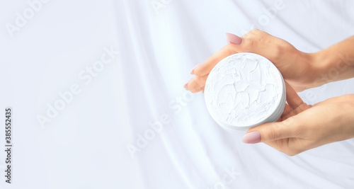 Fototapeta Naklejka Na Ścianę i Meble -  Hands with an open jar of cream on a white silk background. Copy space