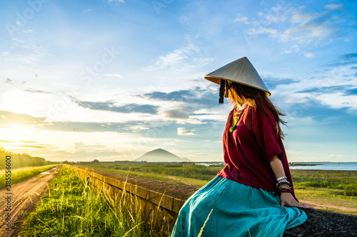 Vietnamese girl sitting on the dike in beautiful sunset with blue sky in Dau Tieng lake  Tay Ninh province  Vietnam.