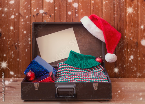 Old briefcase with christmas presents and woolen sweater, fluffy Santa hat and empty card for your text.
