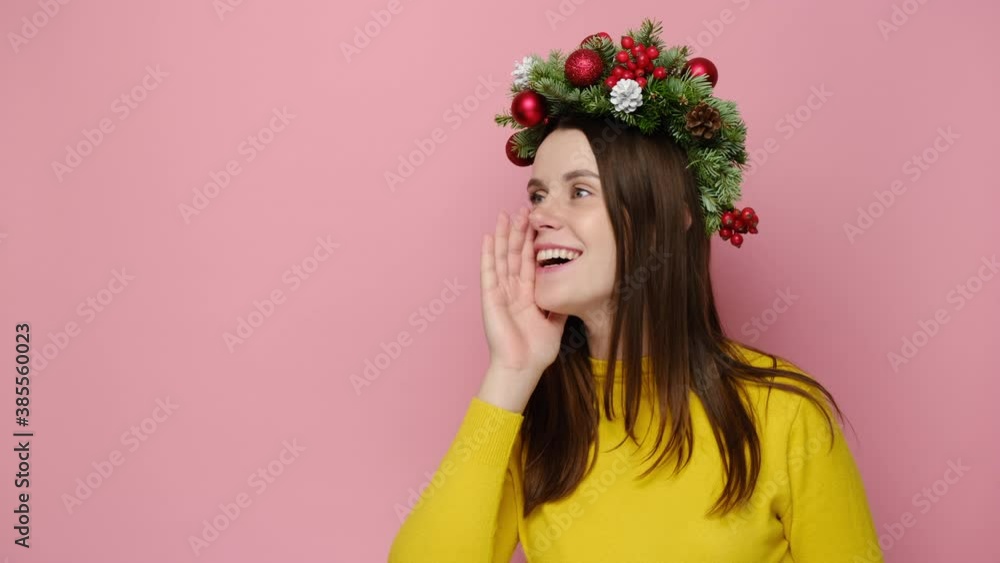 Young woman in traditional Christmas wreath screaming hot news with hand at mouth, isolated on pink studio wall with copy space for advertisement. Happy New Year celebration merry holiday concept Young woman in traditional Christmas wreath screaming hot news with hand at mouth, isolated on pink studio wall with copy space for advertisement. Happy New Year celebration merry holiday concept