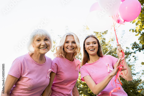 Three women with ribbons of breast cancer awareness near balloons outdoors