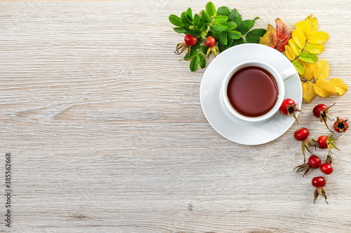 Tea with fresh rosehip berries on a wooden surface with space for text.