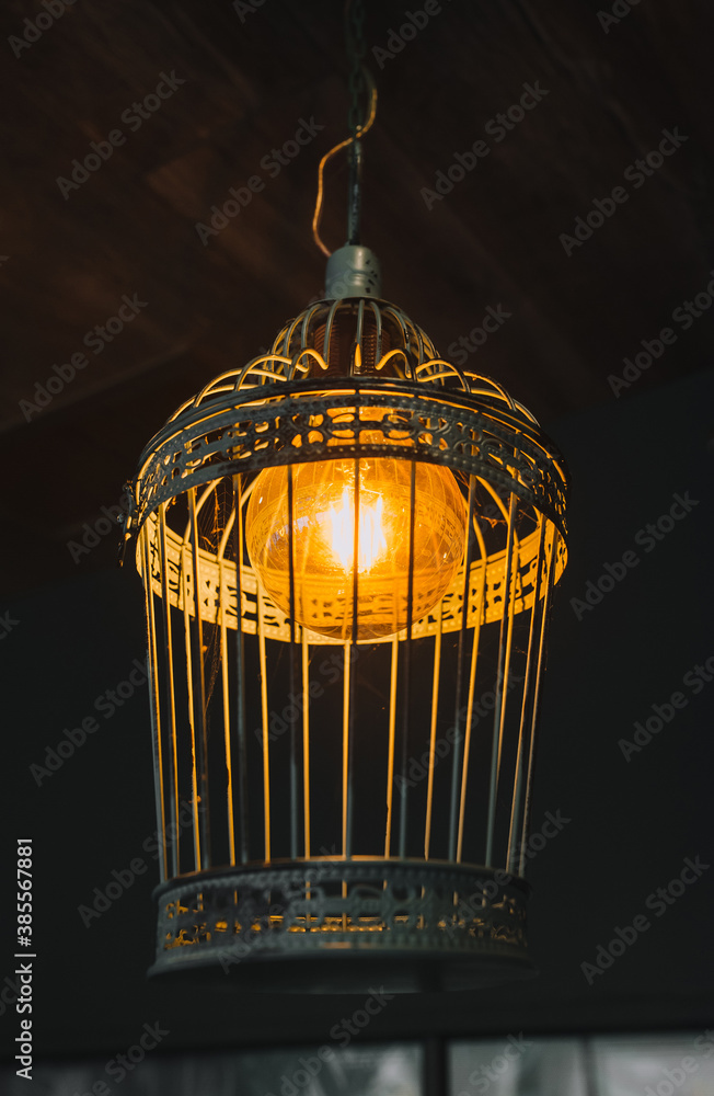 A beautiful metal lamp in the form of a cage with an electric lamp hanging as a decoration on the ceiling close-up.