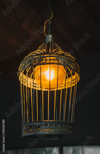 A beautiful metal lamp in the form of a cage with an electric lamp hanging as a decoration on the ceiling close-up. © shchus