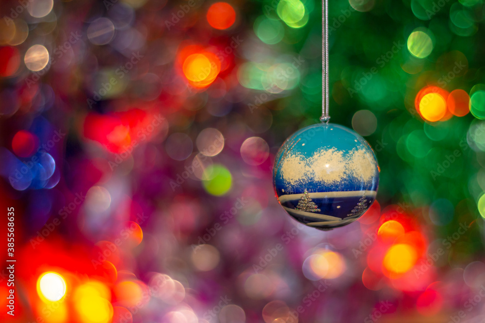 Fototapeta premium A Christmas tree toy ball on a background of multicolored tinsel and a glowing garland.