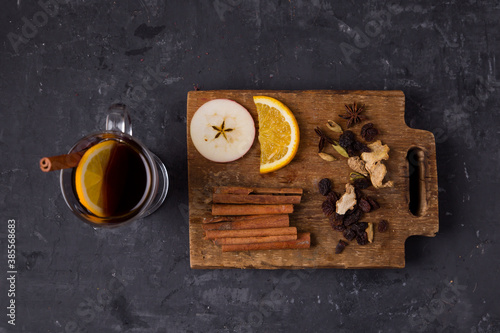 Mulled wine in a glass, ingredients on a wooden board cinnamon sticks, raisins, anise, orange, apple on a gray background. Christmas homemade drink. View from above