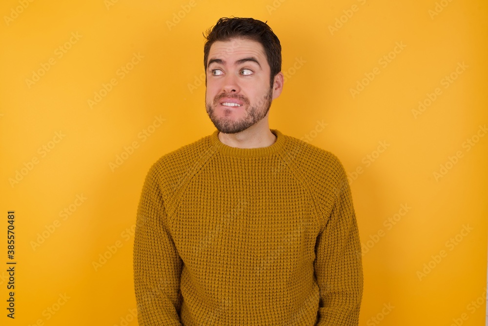 Amazed Young man wearing casual sweater and over isolated yellow background bitting lip and looking up to empty space, Amazed Young man wearing casual sweater and over isolated yellow background bitting lip and looking up to empty space,