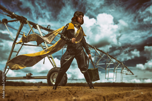 Epic scene of a beautiful young female pilot in front of a vintage airplane, holding a morse code device, her long scarf floating in the wind, on a cloudy day