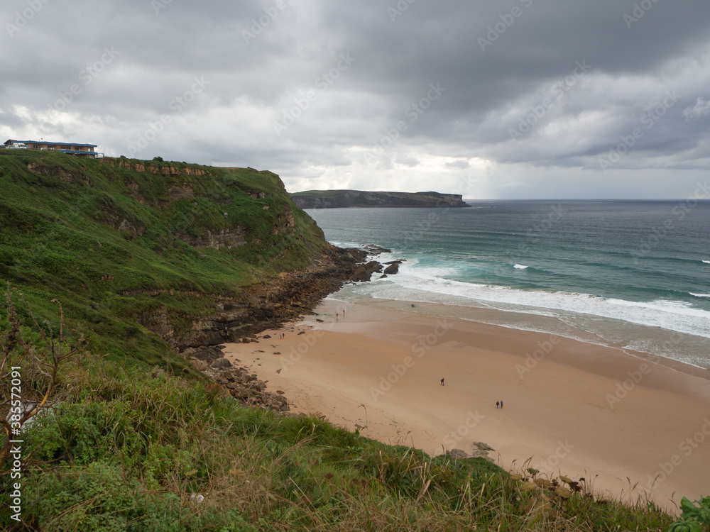 Beach with green cliffs under a cloudy sky