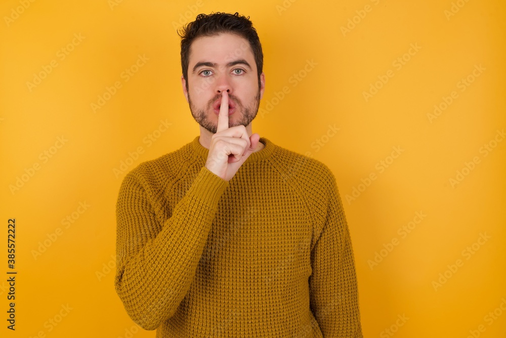 Young man wearing casual sweater and over isolated yellow background asking to be quiet with finger on lips. Silence and secret concept. Young man wearing casual sweater and over isolated yellow background asking to be quiet with finger on lips. Silence and secret concept.
