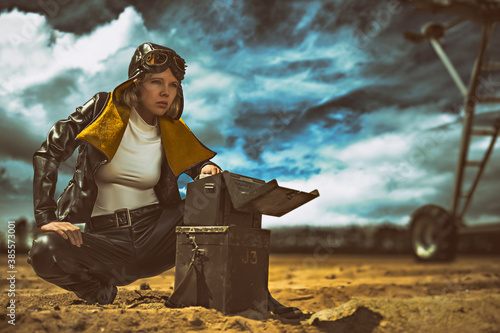 Beautiful young female pilot in front of a vintage airplane, trying to communicate with a morse code device on a cloudy day