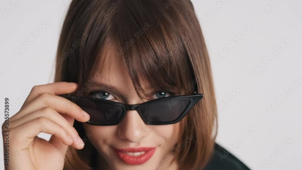 Close up stylish blue eyed girl with bob hair and red lips wearing sunglasses confidently looking in camera isolated on white background Close up stylish blue eyed girl with bob hair and red lips wearing sunglasses confidently looking in camera isolated on white background