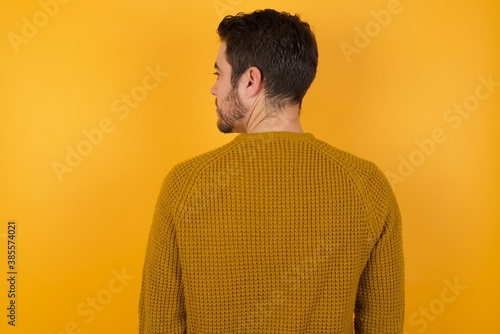 The back side view of a Young man wearing casual sweater and over isolated yellow background Studio Shoot.