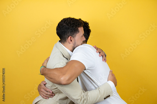 Young gay couple of two men wearing casual clothes over isolated yellow background Standing with smile on face hugging © Irene